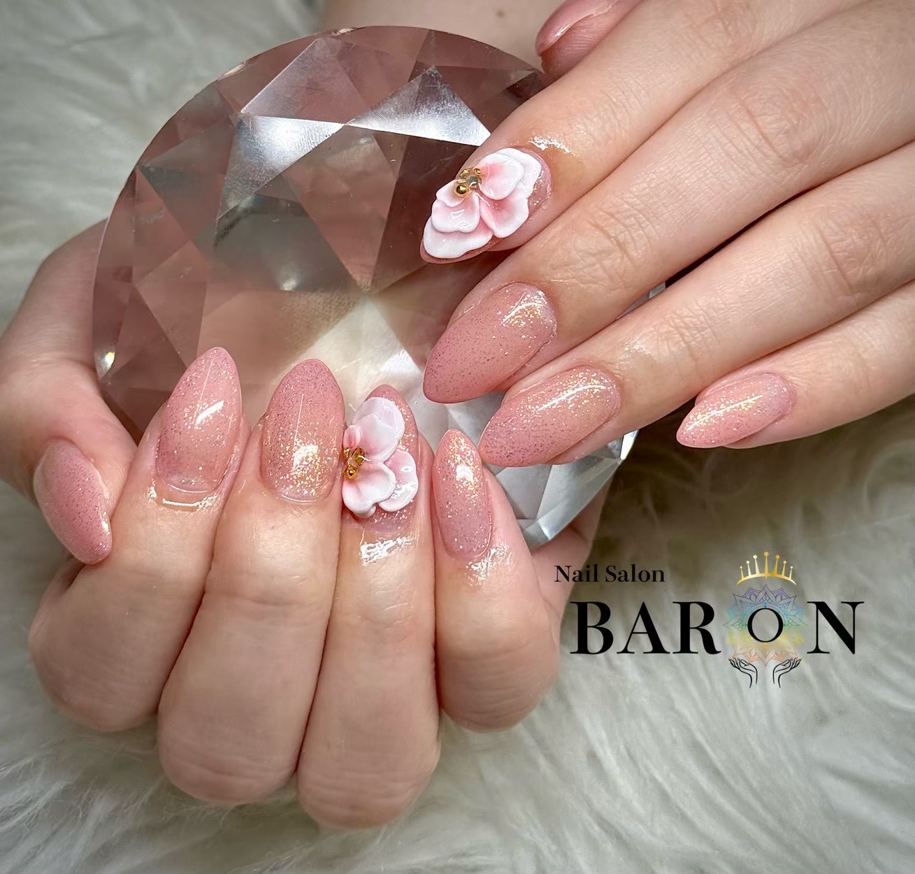 ピンクのラメベースに白と淡いピンクの大きな花びらが重なる、BARONの立体的なフラワーネイル