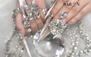 透けるロングネイルに白いライン、蝶や大粒ビジューと揺れる装飾を合わせたBARON町田店の掲載デザイン